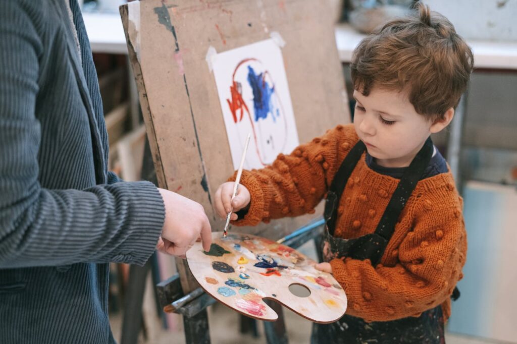 pexels-photo-6816531 Young boy learning to paint with teacher's guidance during art class.